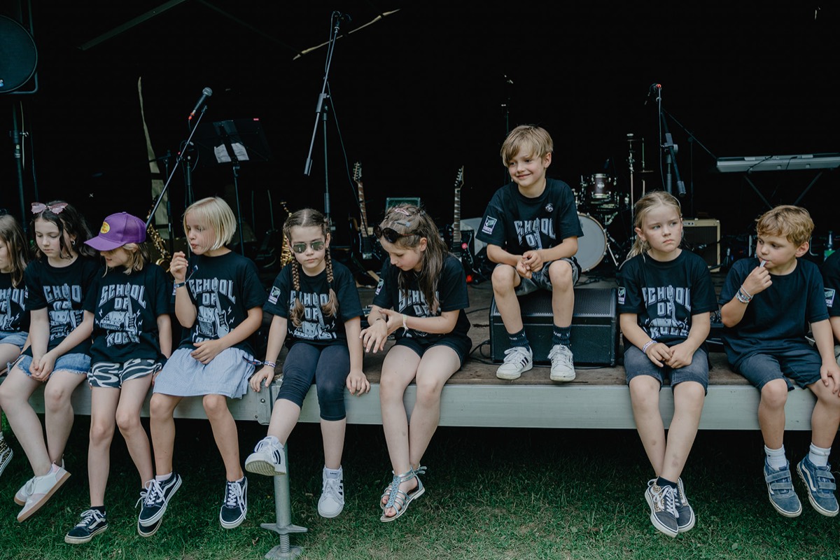 Bandkids in School-of-Rock-Shirts sitzen auf der Bühnenkante