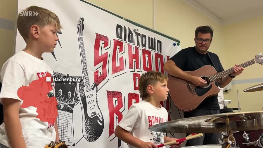 Standbild aus dem SWR-Landesschau-Beitrag: Grundschulrocker vor dem Oldtown-School-of-Rock-Banner